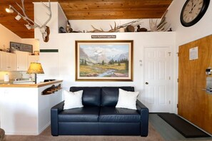 Living space featuring a dark leather loveseat below a mountain landscape painting. - Whitefish Lake Condo w/ Dock & Pool (Whitefish)