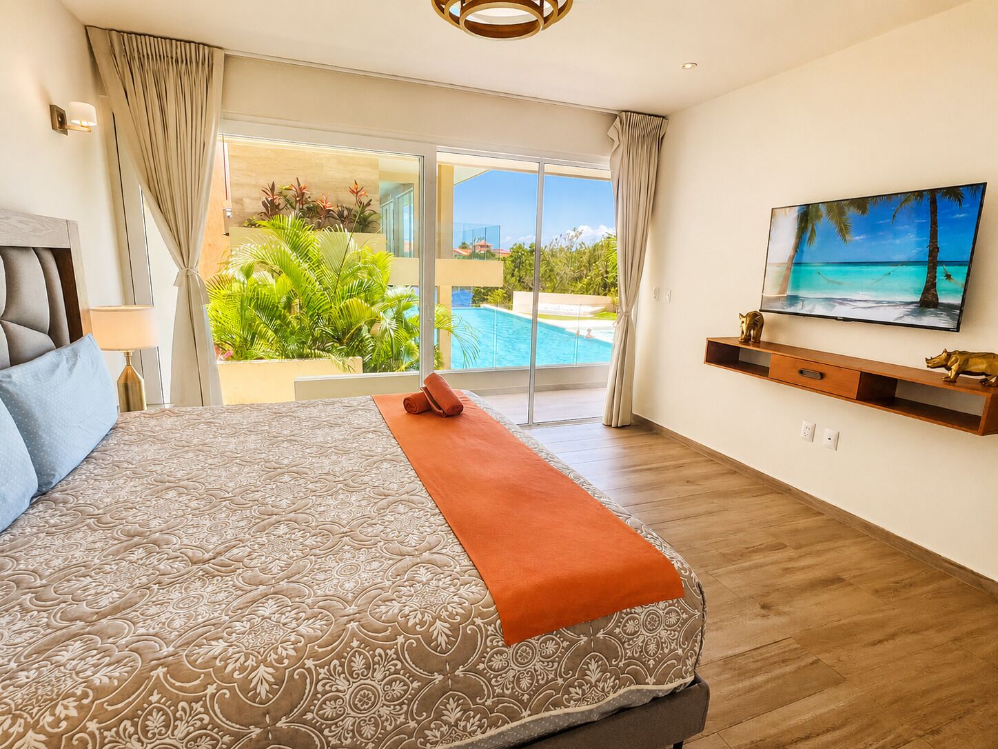 A bedroom with a large bed, a TV, a sliding glass door to a pool, and a view of the outdoors.
