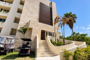Un edifici modern amb una escala que condueix a l'entrada, envoltat de palmeres i un vehicle cobert.