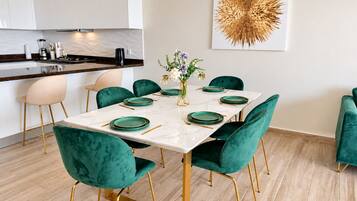 A modern dining area with a marble table, teal velvet chairs, and gold accents.