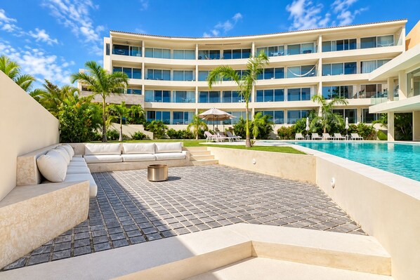 A hotel with a pool, outdoor seating, and a multi-story building. - Marina view 3BR pool 7min walk to beach (Puerto Aventuras)