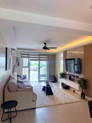 Een moderne woonkamer met een bank, televisie, plafondventilator en een uitzicht door grote glazen deuren.