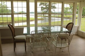Un comedor con una mesa de vidrio y sillas de metal, ventanas amplias con vista a un lago y un parque.
