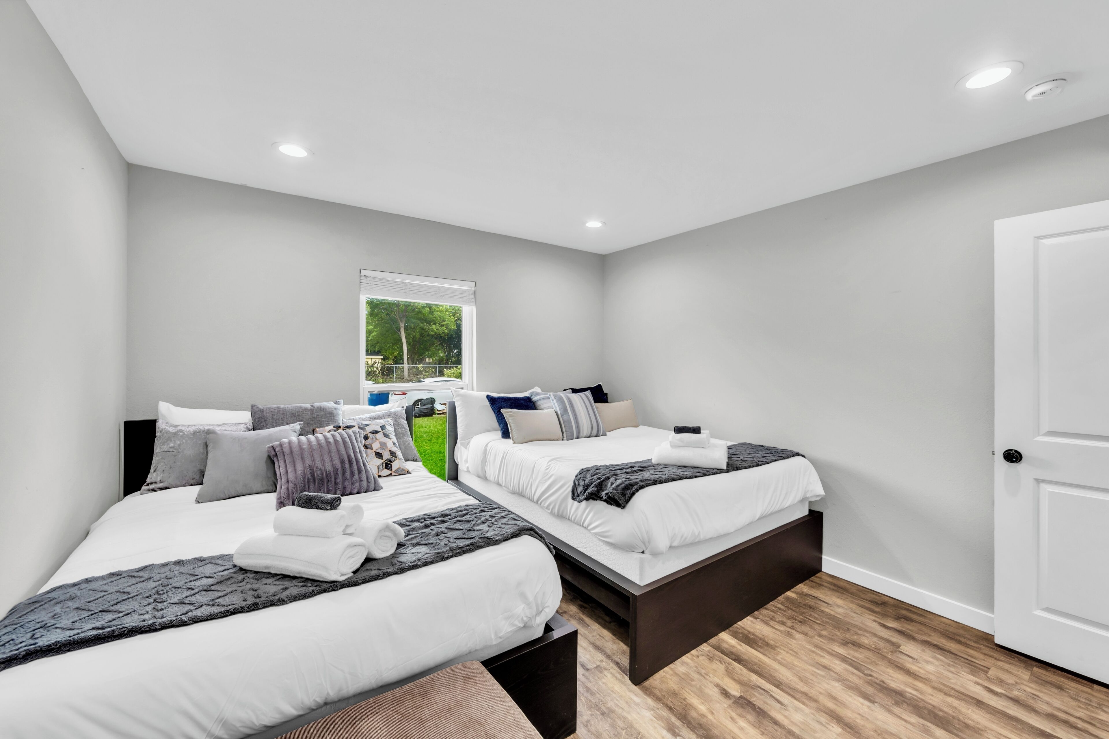 A bedroom with two beds, a window, and a door.