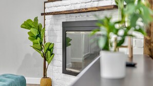 A modern living room with a white brick fireplace, a wooden mantel, and a potted plant. - 3BR Home Near Outlets & Event Center ,
Pet Friendly, Backyard (Allen)