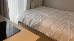 Ein Schlafzimmer mit Bett, Nachttisch, Fenster mit Vorhängen und einer Klimaanlage.