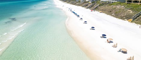 A beach with clear turquoise water, white sand, and a row of beach umbrellas.