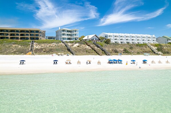 Ein Strandhotel mit mehreren Gebäuden, einem Sandstrand und klarem, blauem Wasser.