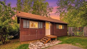 A wooden cabin with a front door, two windows, and a set of stairs leading to the entrance. - Cozy Anchorage Cabin, Full Kitchen & Deck (Anchorage)