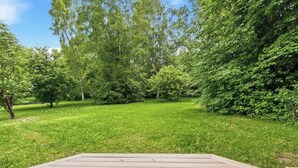 A grassy outdoor area with trees and a wooden deck. - Cozy Anchorage Cabin, Full Kitchen & Deck (Anchorage)