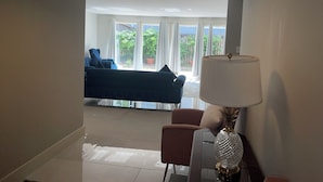 A modern living room with a sofa, a chair, a lamp, and a view of the outdoors through large windows. - Prime  Bethesda Location Easy Access to DC (Bethesda)