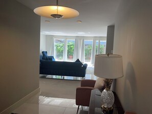 Ein modernes Wohnzimmer mit einer Couch, einem Sessel, einer Lampe und Blick ins Freie durch große Fenster.