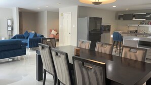 A modern living room with a dark wooden dining table, light-colored chairs, a blue sofa, and a kitchen area with a refrigerator and stove. - Prime  Bethesda Location Easy Access to DC (Bethesda)