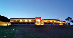 A multi-story building with illuminated windows and a flat roof, situated on a grassy hill. - Mildiss Hotel BW Signature Collection (Besse-et-Saint-Anastaise)