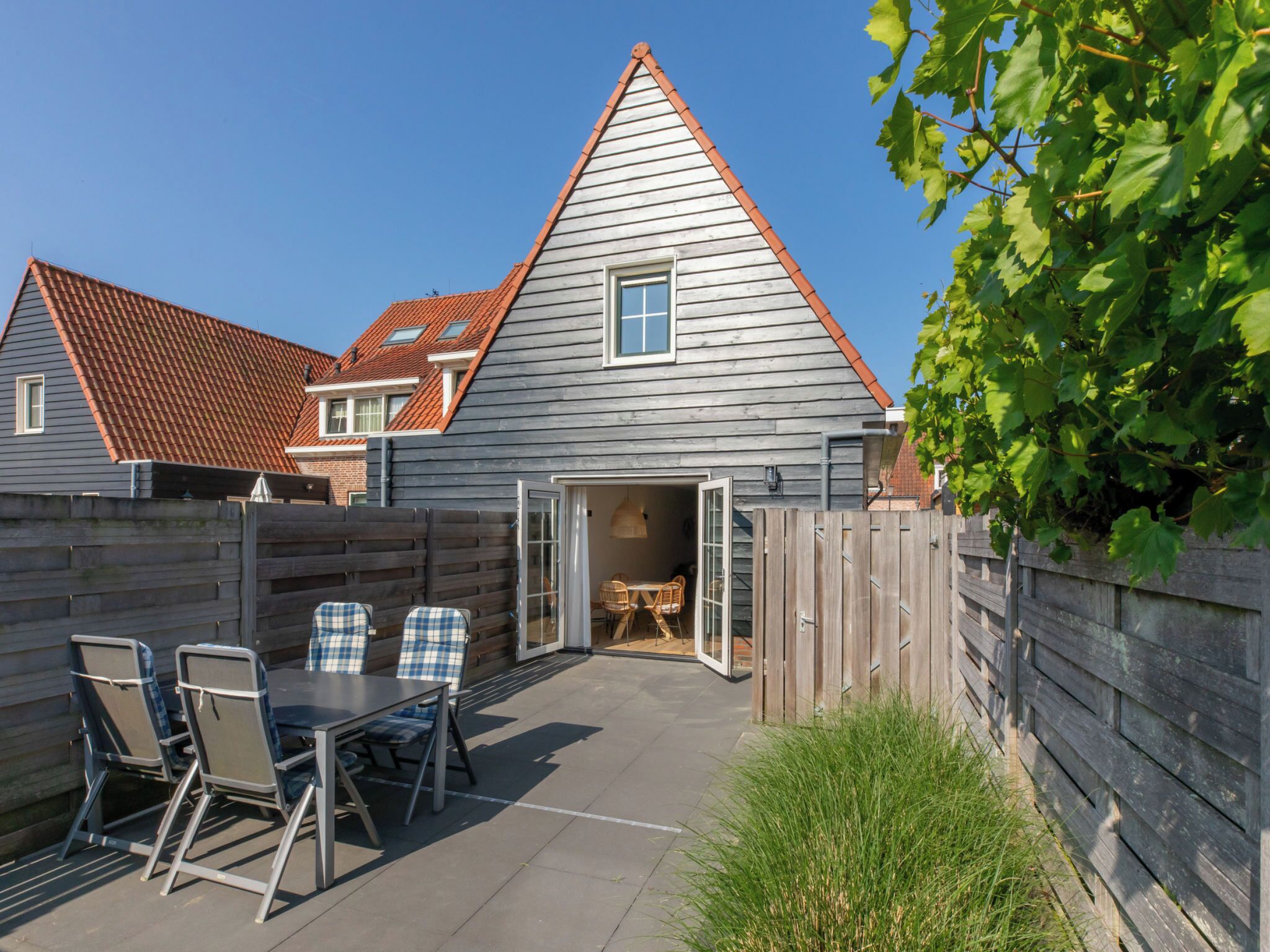 Une maison avec un toit en pente, une clôture en bois et une terrasse avec une table et des chaises.