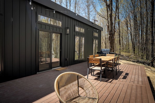 Eine moderne Holzterrasse mit Esstisch, Stühlen, einem Korbstuhl und einem Grill.