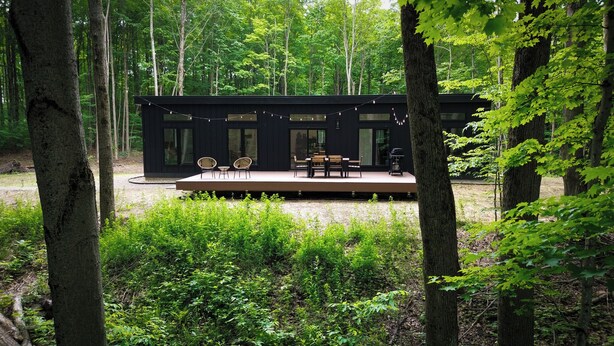 Eine moderne Holzhütte mit einer Terrasse, umgeben von dichtem Wald.