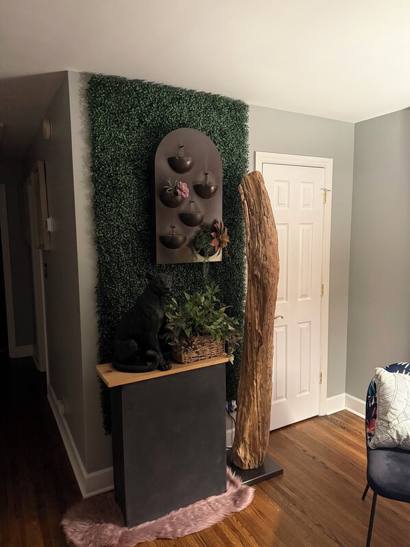 Una habitación con una consola de tonos oscuros, una escultura de gato negro, un estante de pared para plantas y un gran baúl de madera.