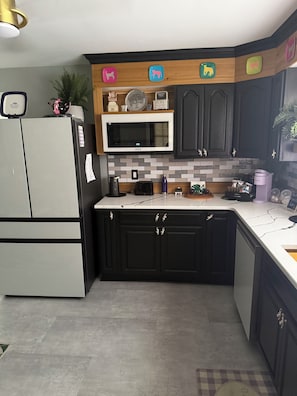 A kitchen with dark cabinets, a microwave, a refrigerator, and a coffee machine.