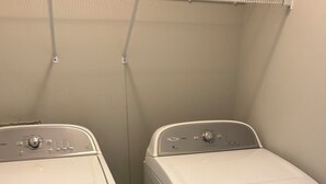 Une buanderie équipée de deux appareils lave-linge et sèche-linge superposés, d’un sol carrelé et d’un mur blanc.