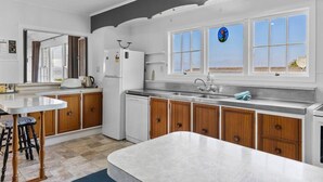 A modern kitchen with a large island, wooden cabinets, a built-in dishwasher, and a view of the beach through the windows. - Relax and Recharge overlooking Lake Taupo (Taupō)