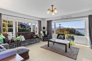 Een ruime woonkamer met een bank, fauteuils, een salontafel en uitzicht op zee.