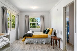 Ein Schlafzimmer mit Bett, Nachttisch, einem Fenster mit Vorhängen und Blick ins Grüne.