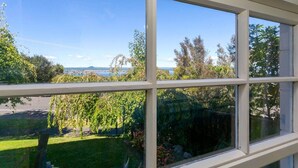 A window with a view of a grassy area, trees, and a distant body of water. - Relax and Recharge overlooking Lake Taupo (Taupō)