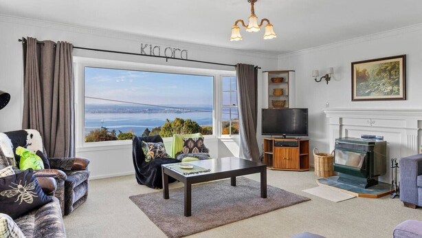 A living room with a large window, a television, a fireplace, and a view of the sea. - Relax and Recharge overlooking Lake Taupo (Taupō)