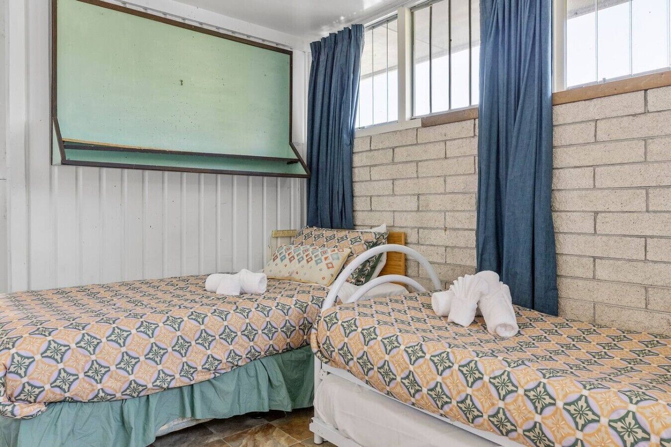 Quarto com duas camas, uma tela de projeção e uma parede de tijolos.
