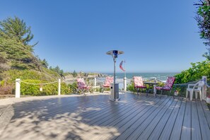 Eine Holzterrasse mit Stühlen und Tisch, mit Blick auf einen Strand und den Ozean.
