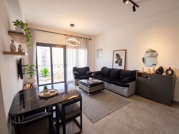 Ein modernes Wohnzimmer mit Sofa, Couchtisch, Fernseher und einem Essbereich mit Tisch und Stühlen.