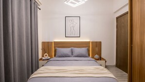 Quarto com cama, cortinas, cabeceira, mesa de cabeceira, cómoda e guarda-roupa.