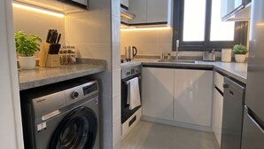 Cozinha moderna com máquina de lavar embutida, eletrodomésticos de aço inoxidável e uma janela que oferece luz natural.
