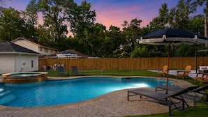 A backyard with a swimming pool, lounge chairs, and a wooden fence. - Spring Oasis: Heated Pool, Spa • Pickleball • Mini Golf • Basketball • Sleeps 12 (Spring)