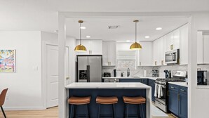 A modern kitchen with a central island, bar stools, pendant lights, and stainless steel appliances. - Spring Oasis: Heated Pool, Spa • Pickleball • Mini Golf • Basketball • Sleeps 12 (Spring)