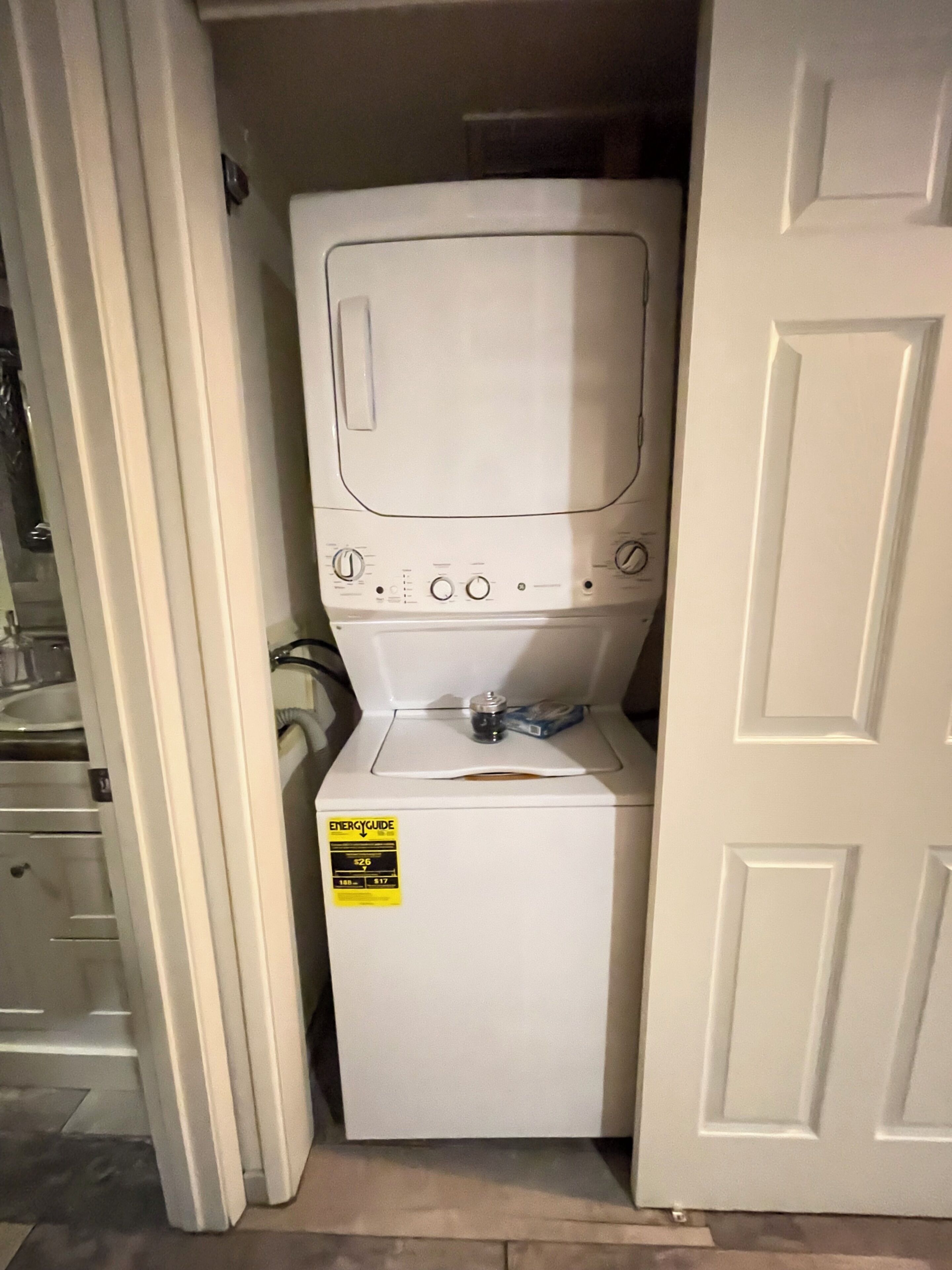 A compact, white laundry machine in a small room with a door on one side.