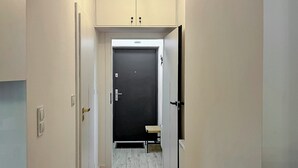 A hallway with a black door, a small bench, and a light switch on the wall. - Nowy Dwór Mazowiecki Chic Studio (Nowy Dwór Mazowiecki)