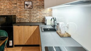 A compact kitchen with a brick wall, a wooden cabinet, a black countertop, a sink, and a green chair. - Nowy Dwór Mazowiecki Chic Studio (Nowy Dwór Mazowiecki)