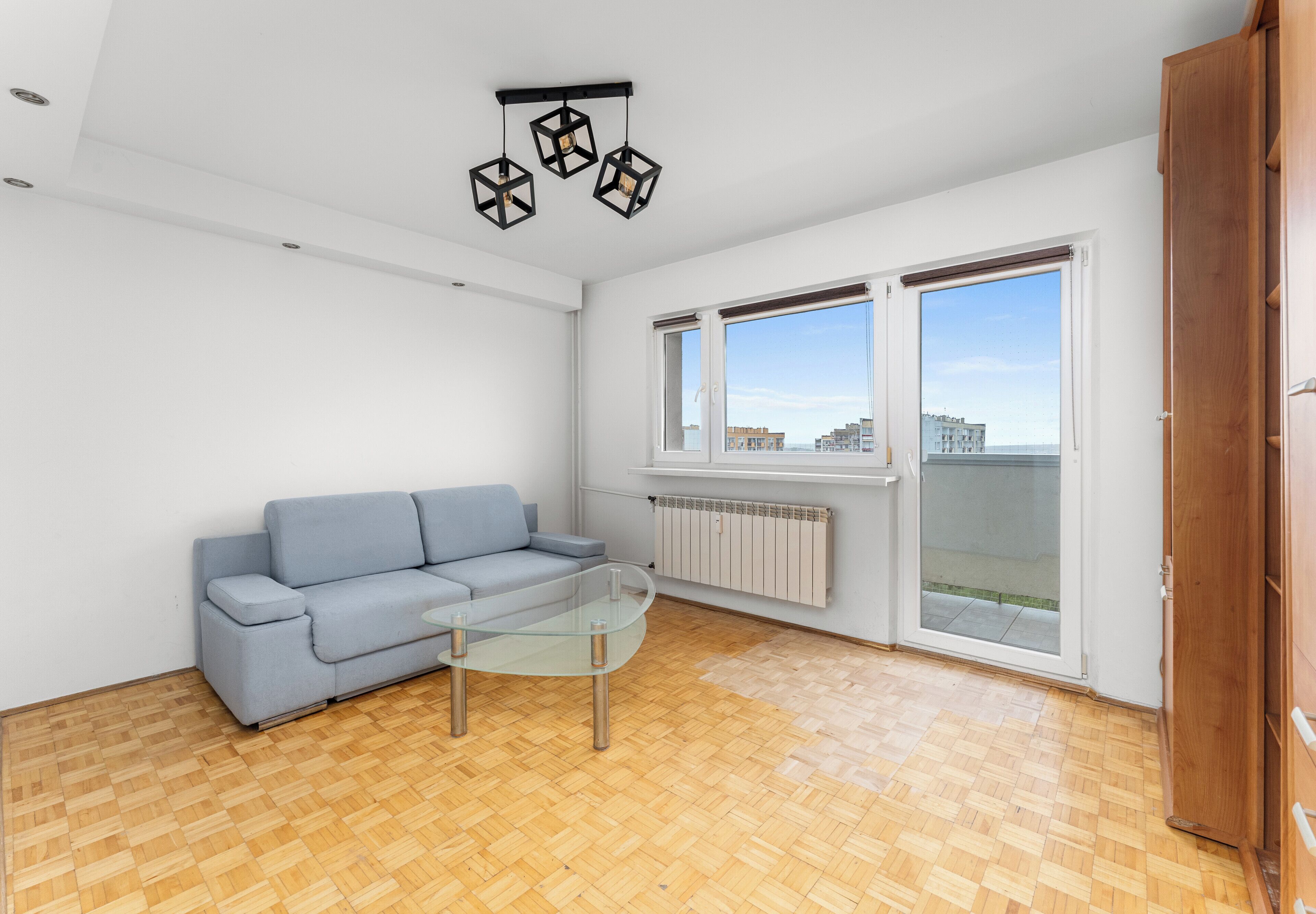 Uma sala de estar moderna com um sofá azul claro, uma mesa de centro de vidro e um chão em assoalho de madeira.