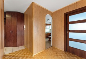 Una habitación con paredes de madera, un armario de madera, una puerta con paneles de vidrio esmerilado y un piso de madera a cuadros.