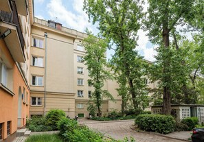 Ein Innenhof mit einem gepflasterten Weg, einem Gebäude mit vielen Fenstern und einem großen Baum.