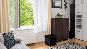 Moderni olohuone, jossa on sohva, pieni musta jakkara, ikkuna verhoilla, kaappi ja peili seinällä.