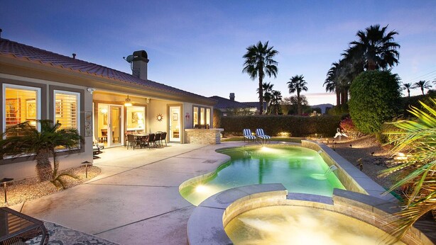Una casa con piscina, mobiliario de patio y palmeras.