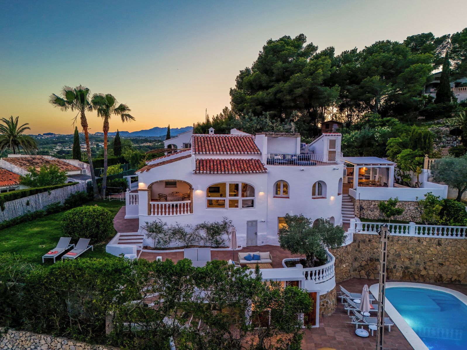 Une villa blanche avec un toit recouvert de tuiles rouges, une piscine et un jardin aménagé.