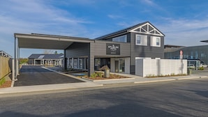A modern hotel with a covered entrance, a signboard, and a gated driveway.