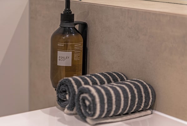 A bottle of Ashley & Co hand wash soap and a rolled towel on a white surface.