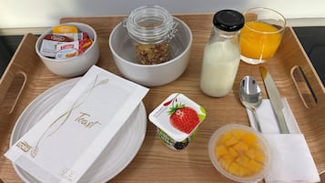 Ein Frühstücksbrett mit Toast, Müsli, Milch, Orangensaft, Joghurt und einer Obstschale.
