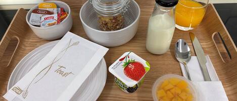 Bandeja de desayuno con tostadas, cereal, leche, jugo de naranja, yogur y un bol de fruta.