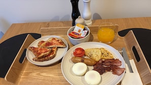A breakfast tray with toast, eggs, bacon, sausages, tomatoes, and a glass of orange juice.